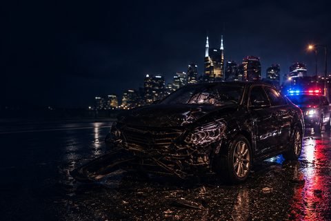Damaged car on a wet road at night, police lights behind it